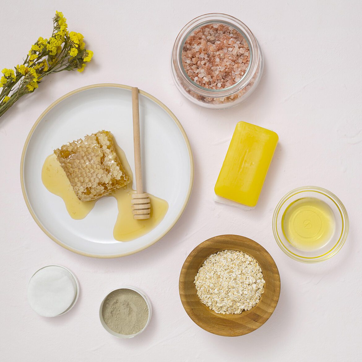 Overhead view yellow flower cotton pads oats essential oil soap himalayan rock salt white textured background