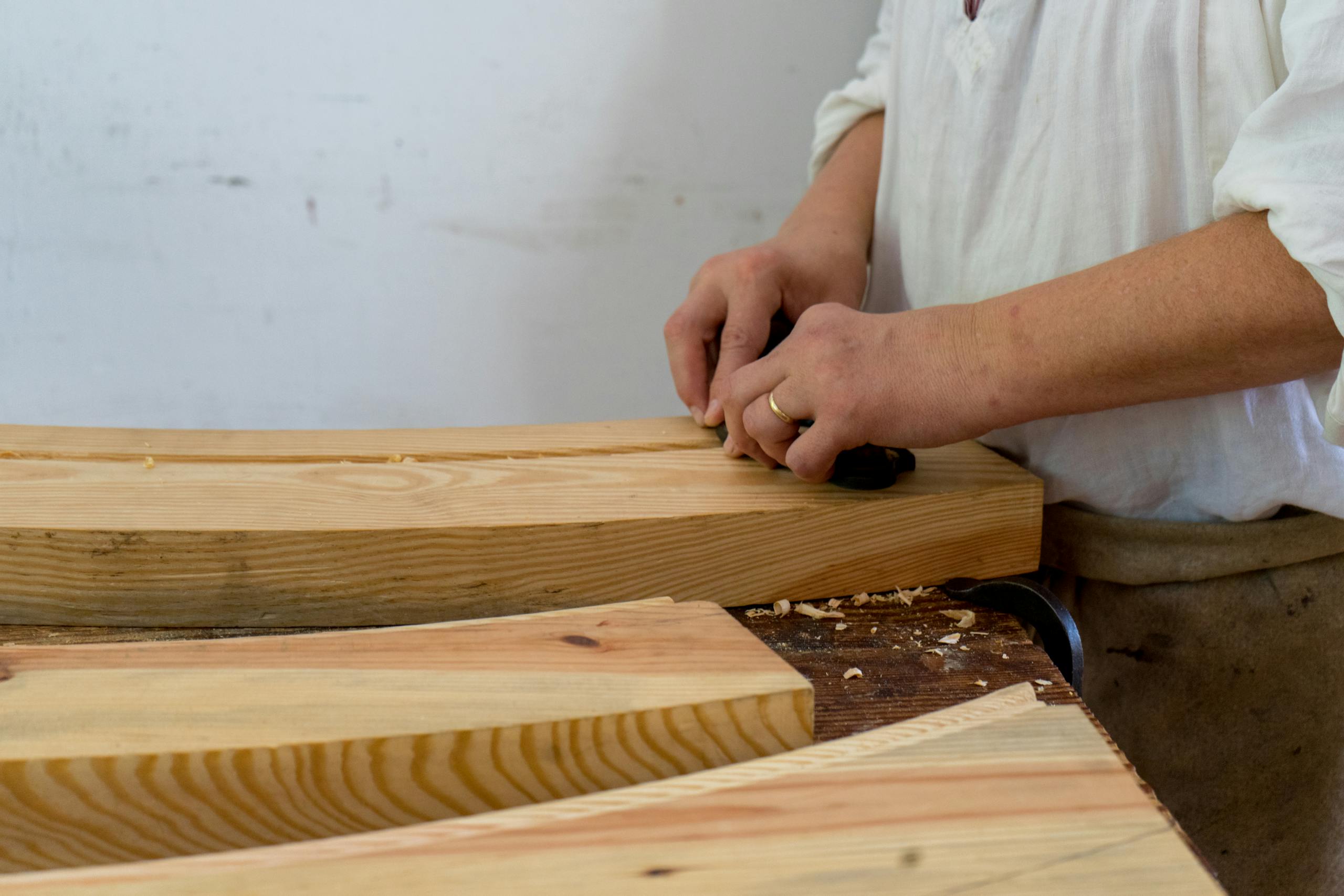A craftsman shaping wooden planks indoors, focusing on precise woodworking techniques.
