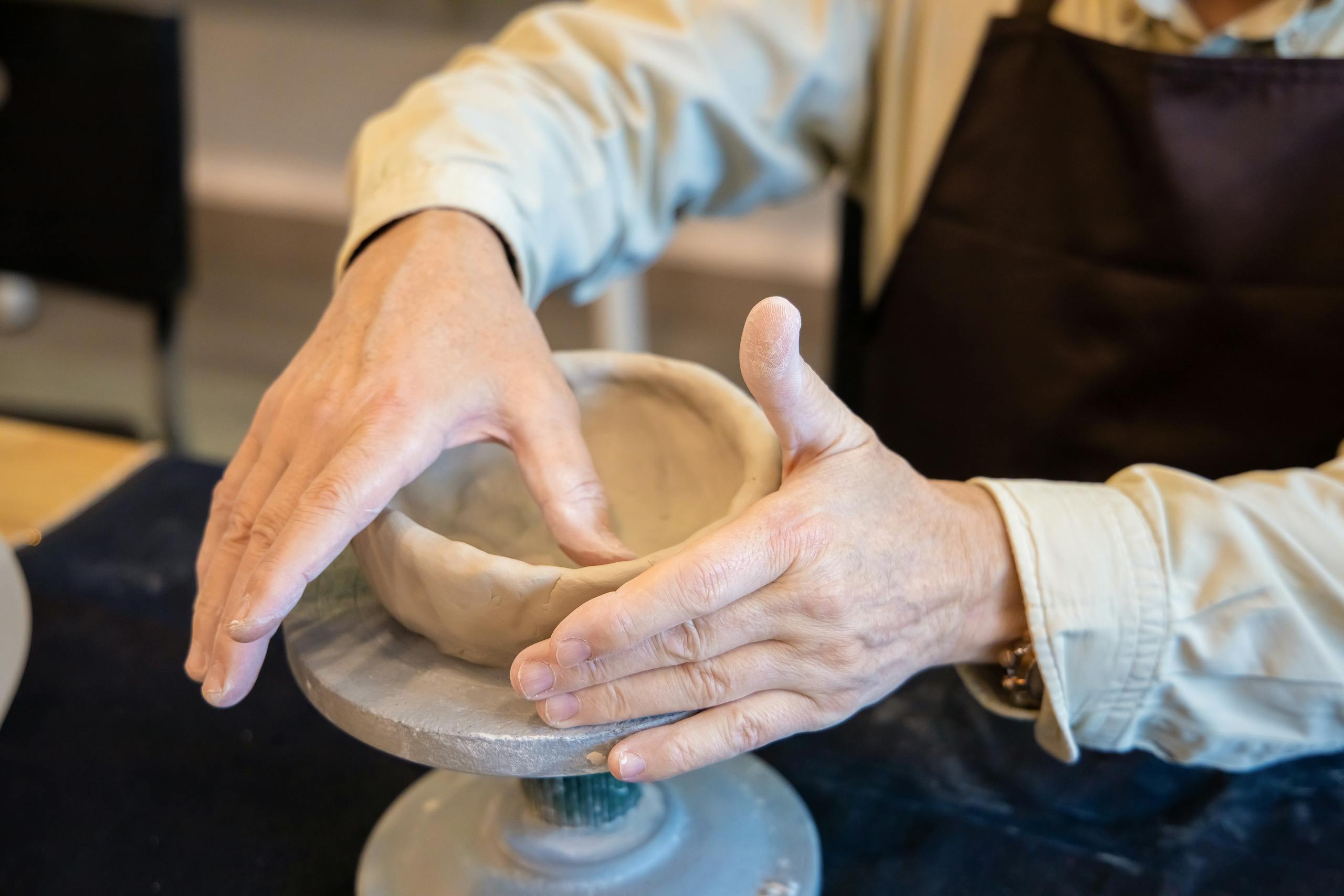 Hands shaping a clay bowl on a pottery wheel, showcasing detailed craftsmanship.