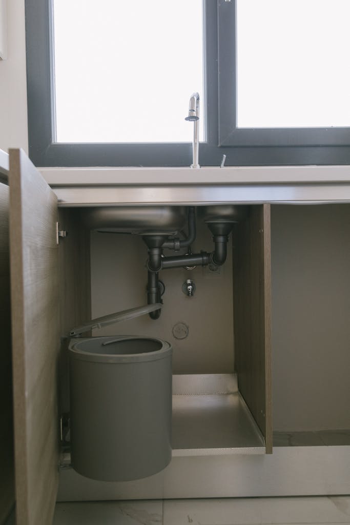 Under-sink view of modern plumbing with garbage bin in an Istanbul apartment kitchen.