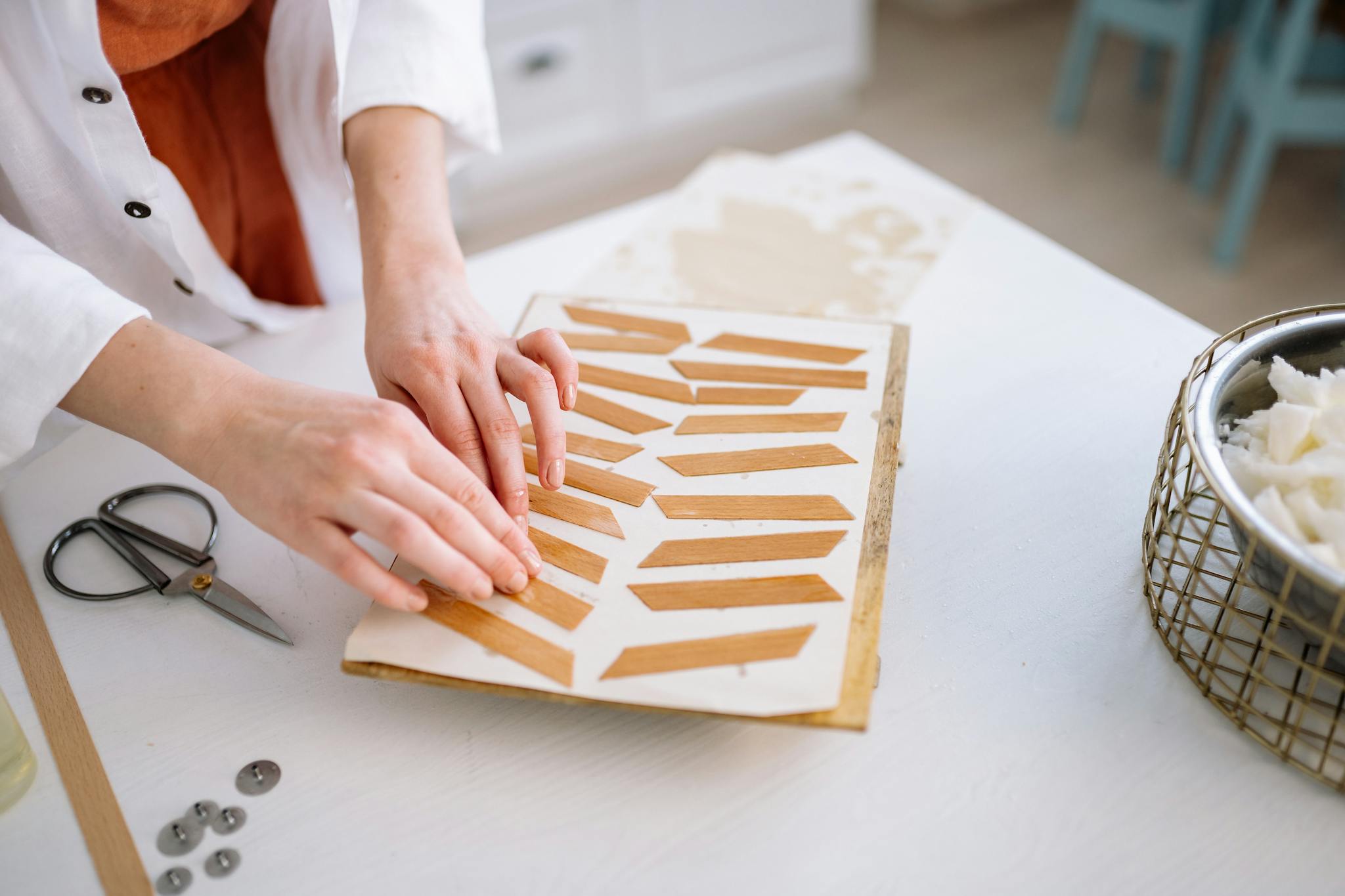 Close-up of hands assembling candle wicks on a wooden tray.