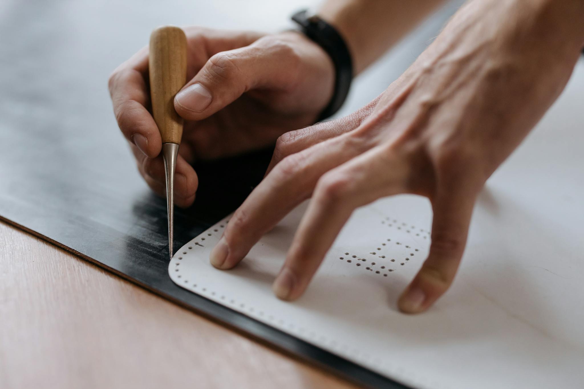 Hands holding a chisel marking paper in a close-up view, showing manual craftsmanship.