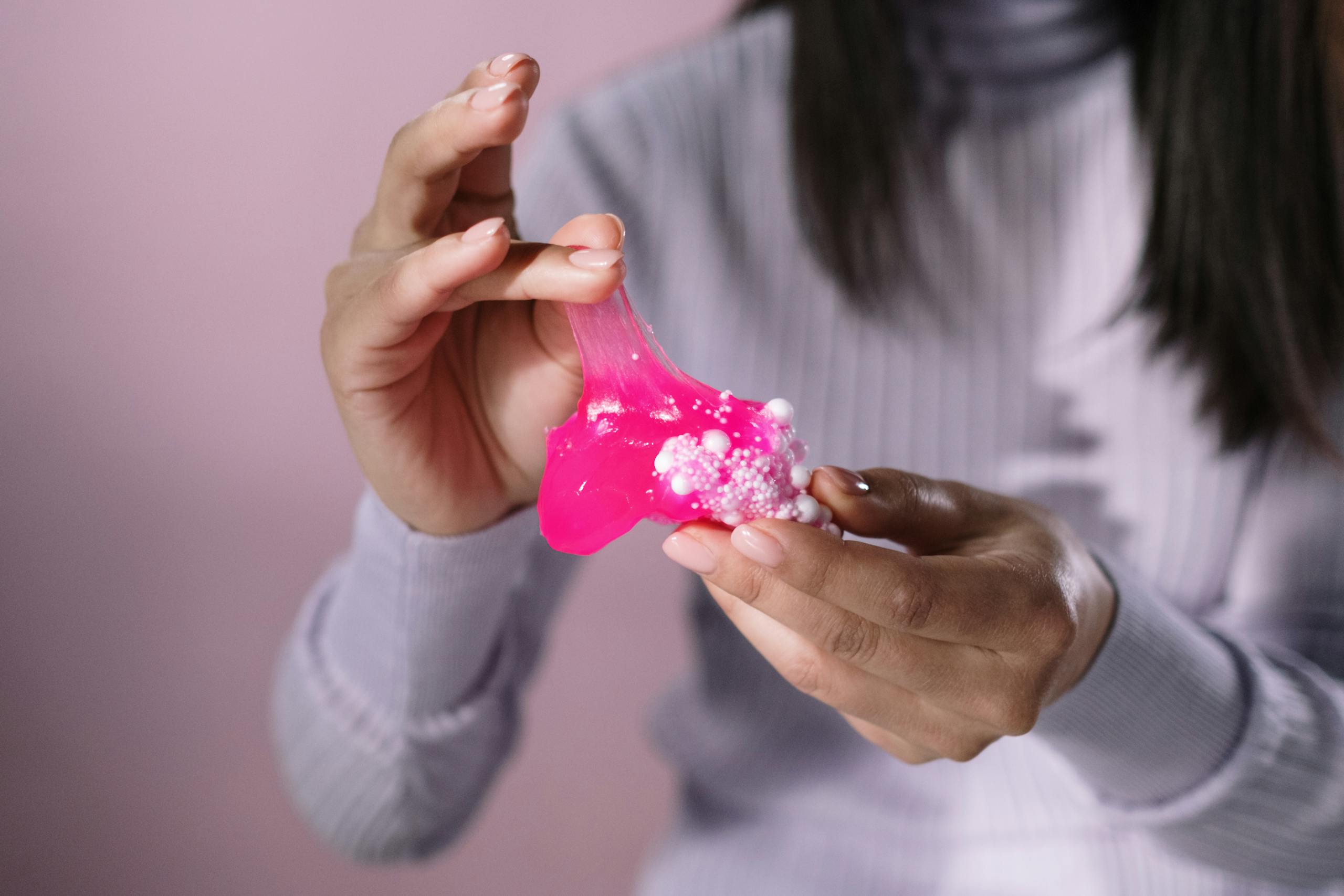 Close-up of hands stretching pink slime with foam beads, showcasing texture and tactile sensation.